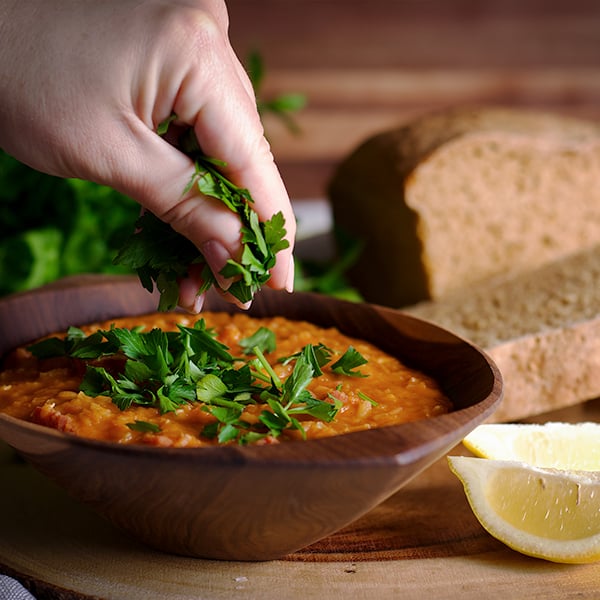 Woman sprinkling fresh herbs on Red Lentil Soup with Ham from A Little and a Lot.