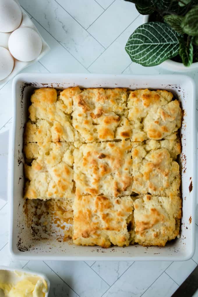 Top down view of butter swim biscuits in a baking dish, next to fresh eggs and a butter dish.