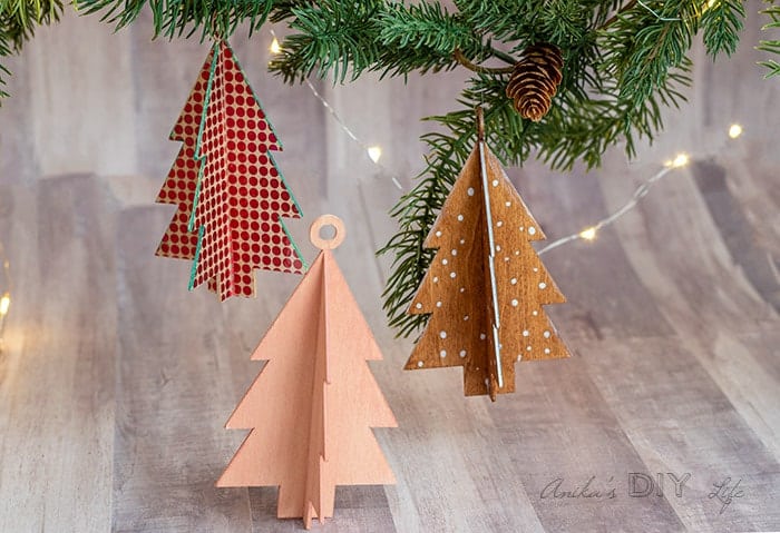 Three dimentional wooden christmas tree ornaments hanging from a Christmas tree.