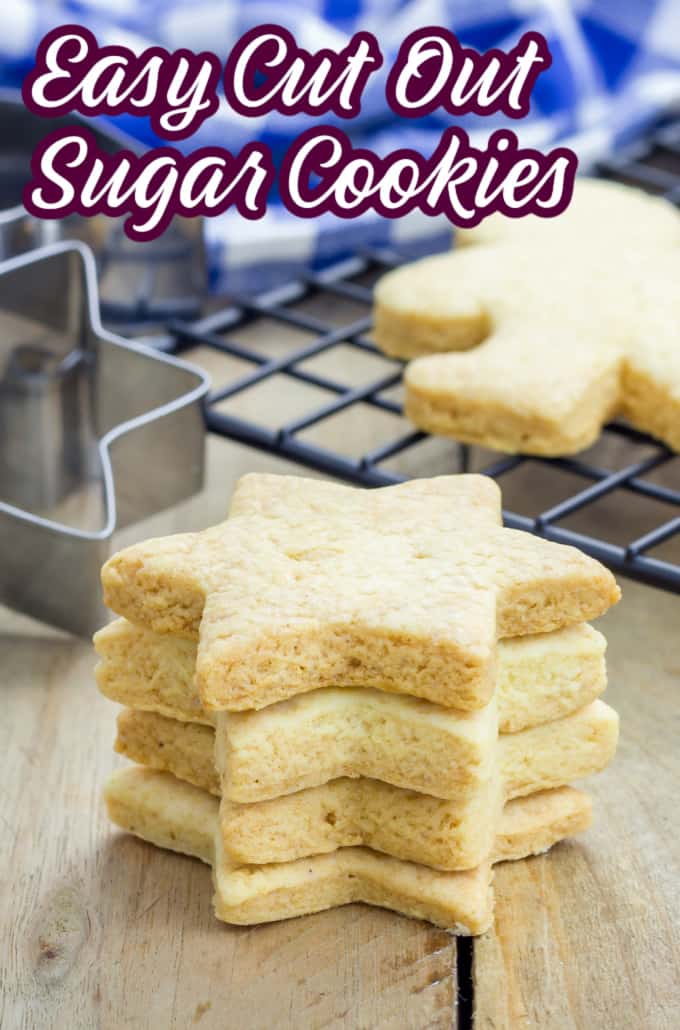 A stack of cut out sugar cookies in front of a cooling rack and cookie cutters.
