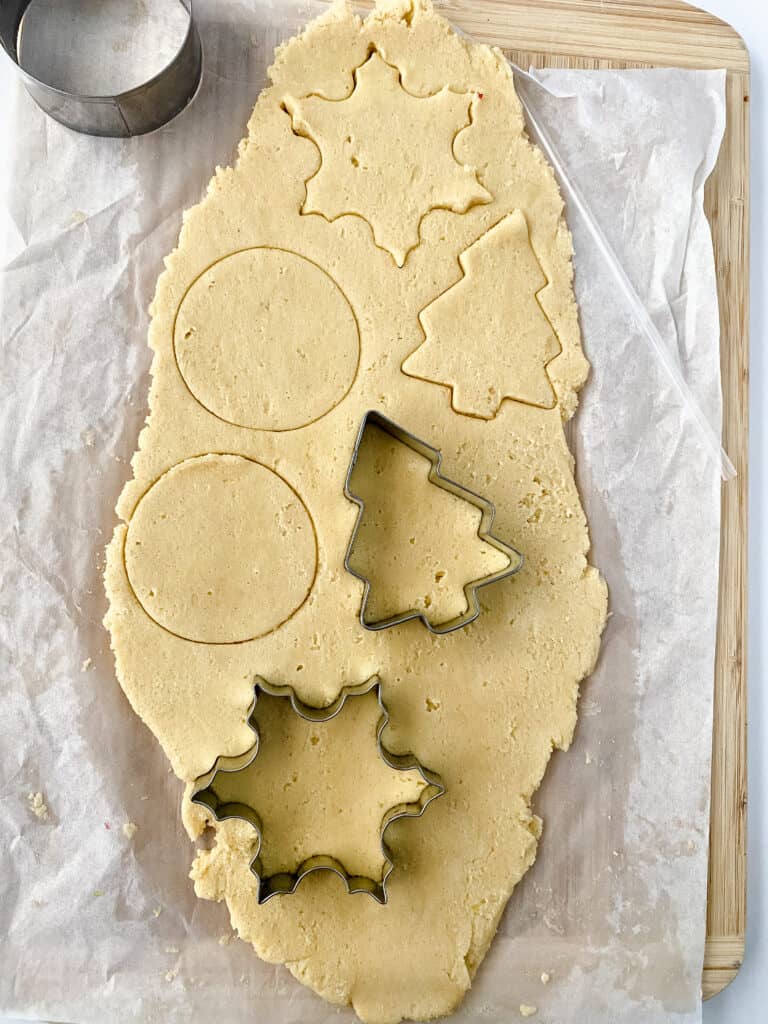 Ornament shaped sugar cookies being cut out of dough.
