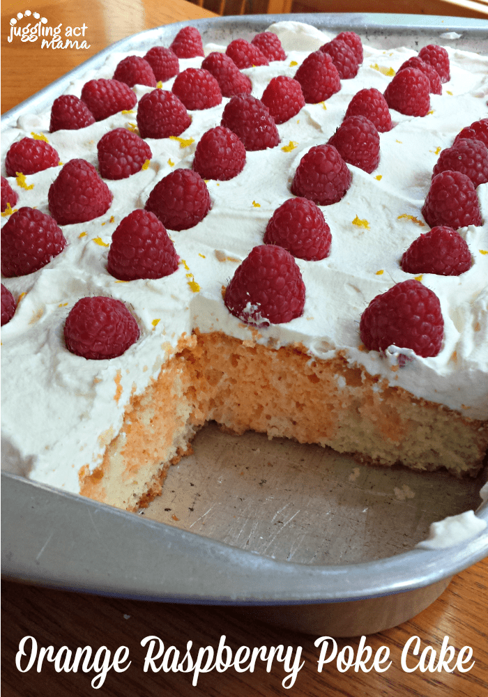 Baking pan of raspberry poke cake with a slice cut out. The cake is topped with whipped cream and fresh berries.
