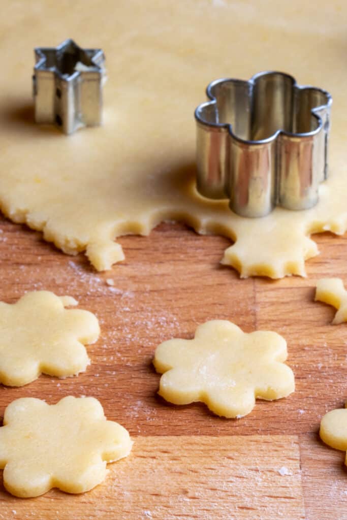 Dough on a butcher block counter top being cut with cookie cutters.
