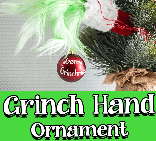 A grinch hand holding an ornament that reads Merry Grinchmas.