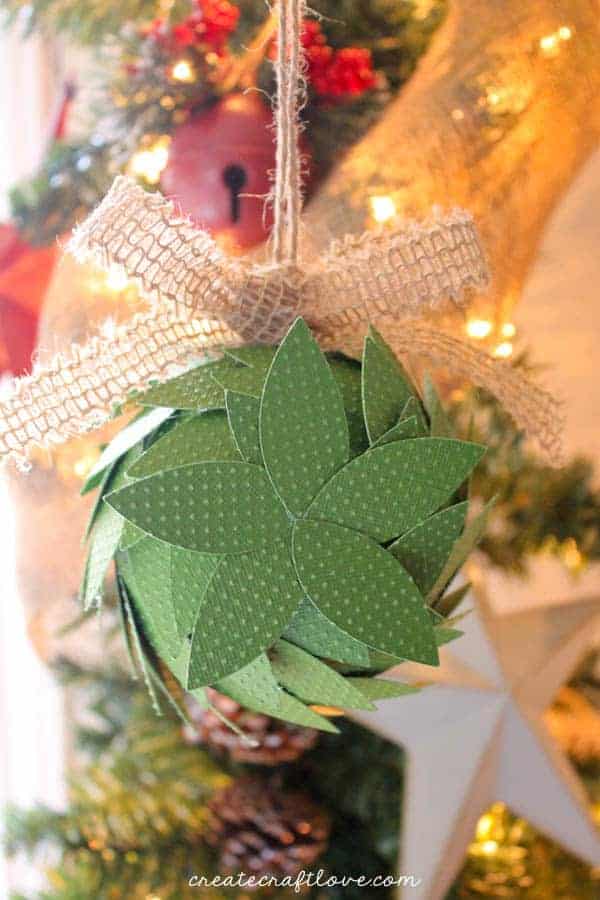 Image contains a holiday kissing ball made from scrapbook paper hanging from a Christmas tree.