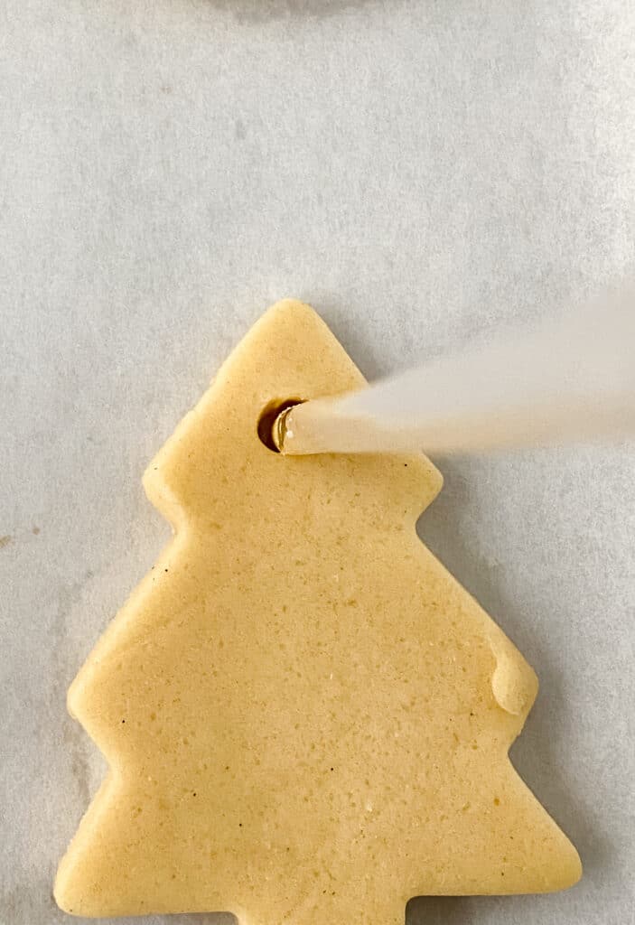 Poking a hole in the top of a sugar cookie.
