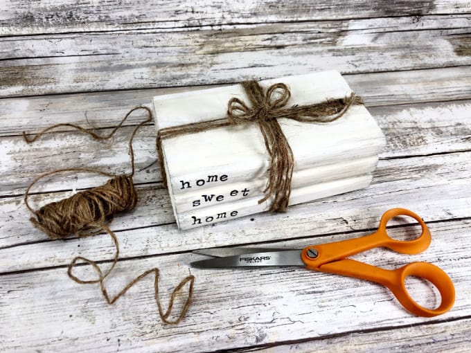 DIY Stacked books tied together with twine next to a spool of twine and craft scissors.