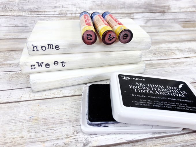 Close up image of faux books painted white, a stamp pad, and the stamps used to create words on the spines.