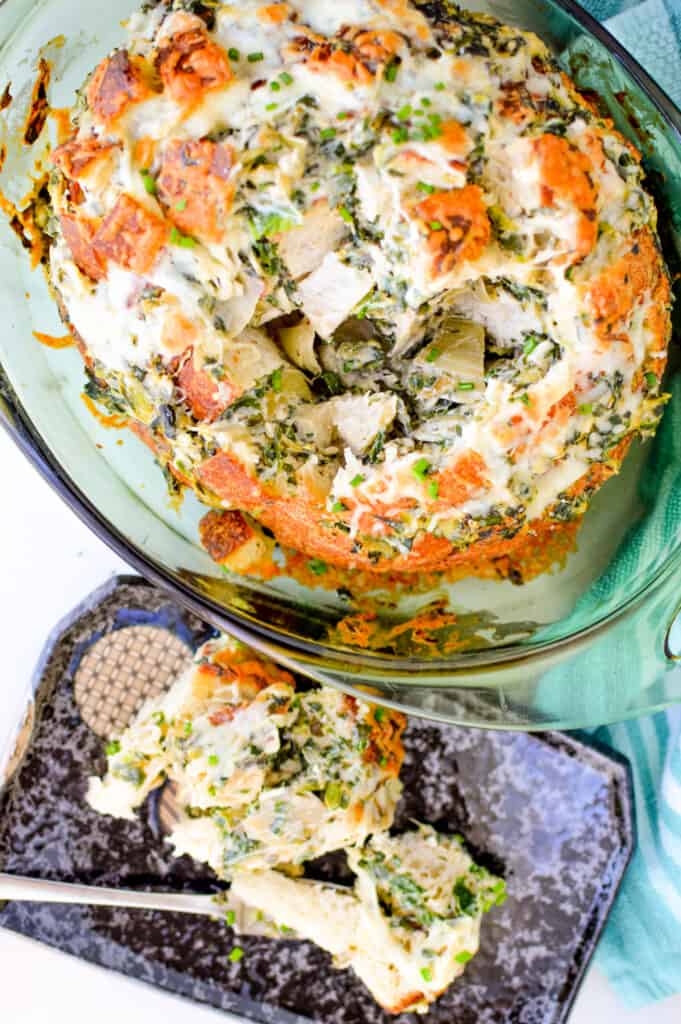 Top down view of spinach and artichoke bread in a baking dish along side a plate filled with pull apart bread and a fork.