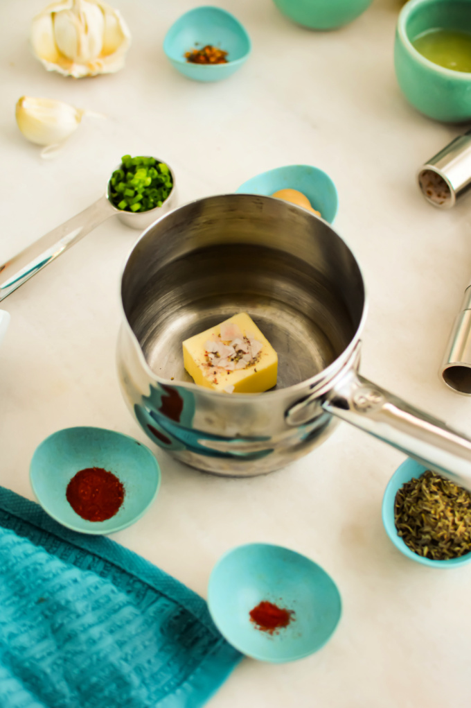Top down view of butter in a saucepan surrounded by ingredients to make cowboy butter dipping sauce.
