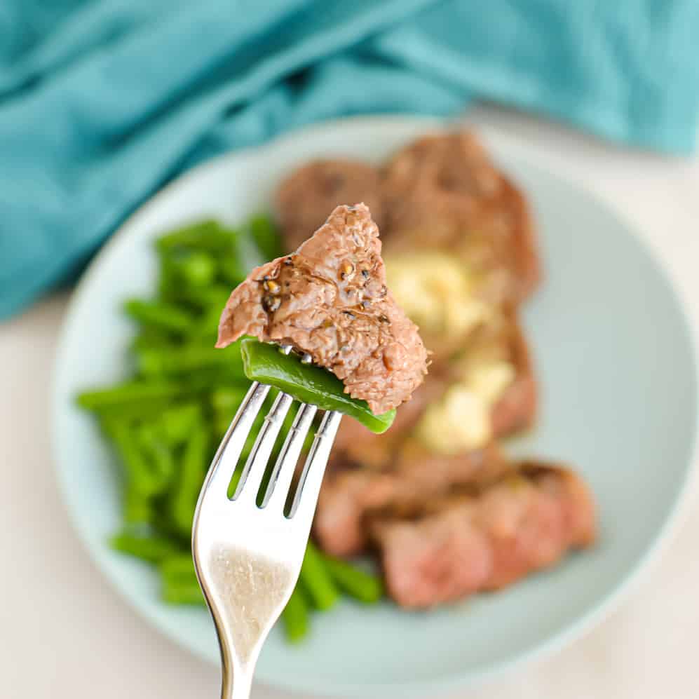 Close up square image of Broiled New York Strip Steak on a fork with a green beans.