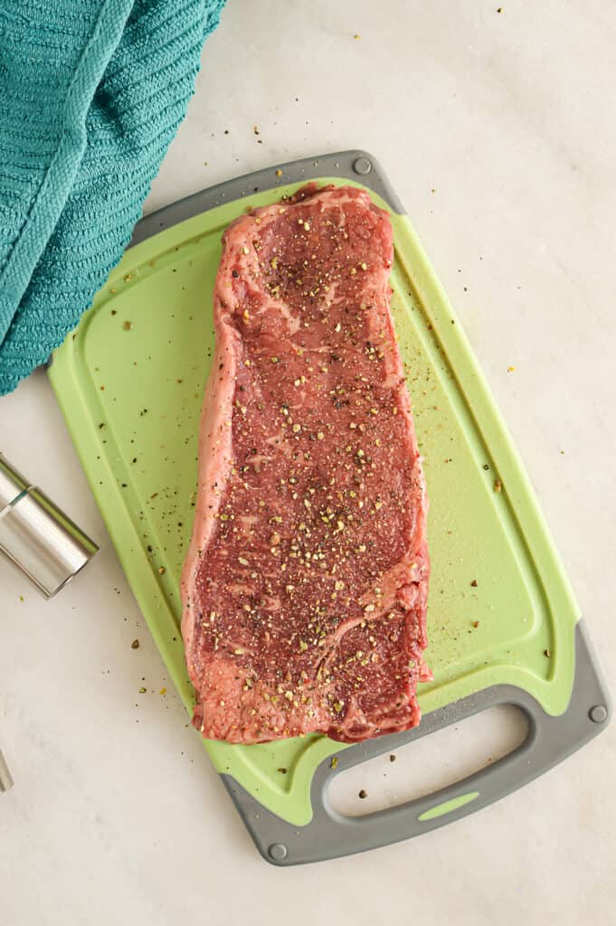 Seasoned New York strip steak on a cutting board.