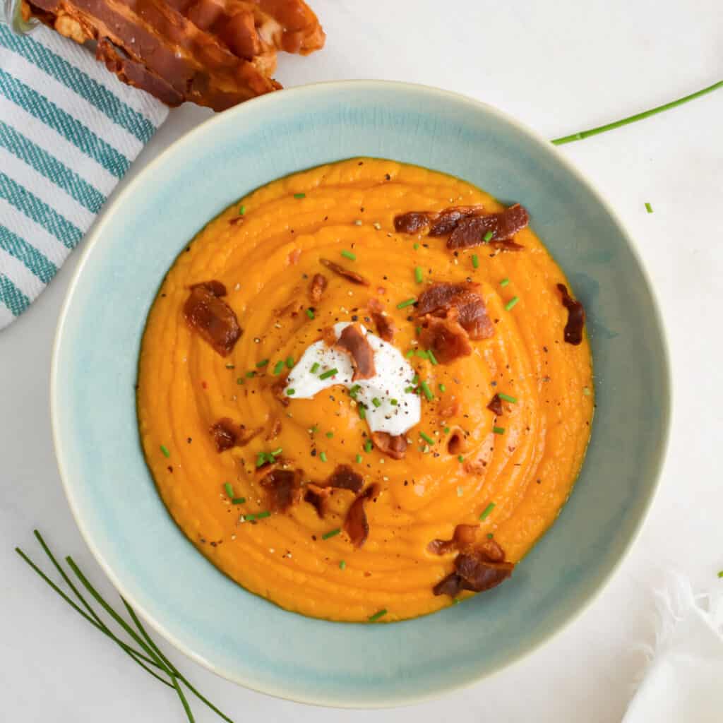 Top down view of Sweet Potato Soup in a bowl topped with crispy bacon, sour cream and green onions.