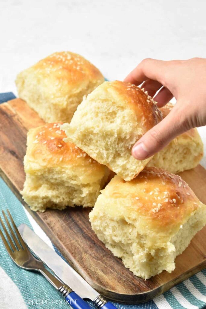 A hand taking a roll from a wooden platter filled with no-knead rolls.