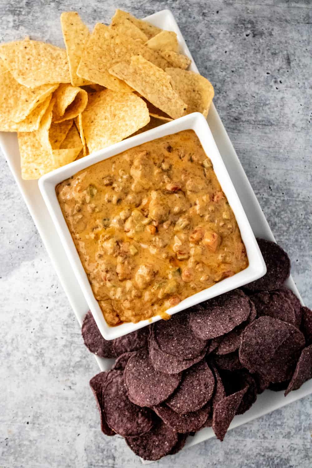 Top down view of Velvetta Queso Dip in a square bowl with tortilla chips and blue corn chips.