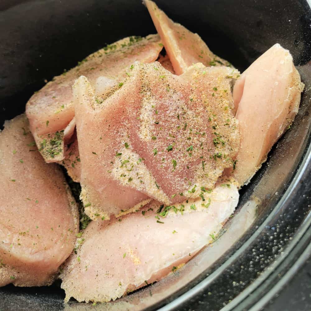 Close up of seasoned frozen chicken in a crock pot.