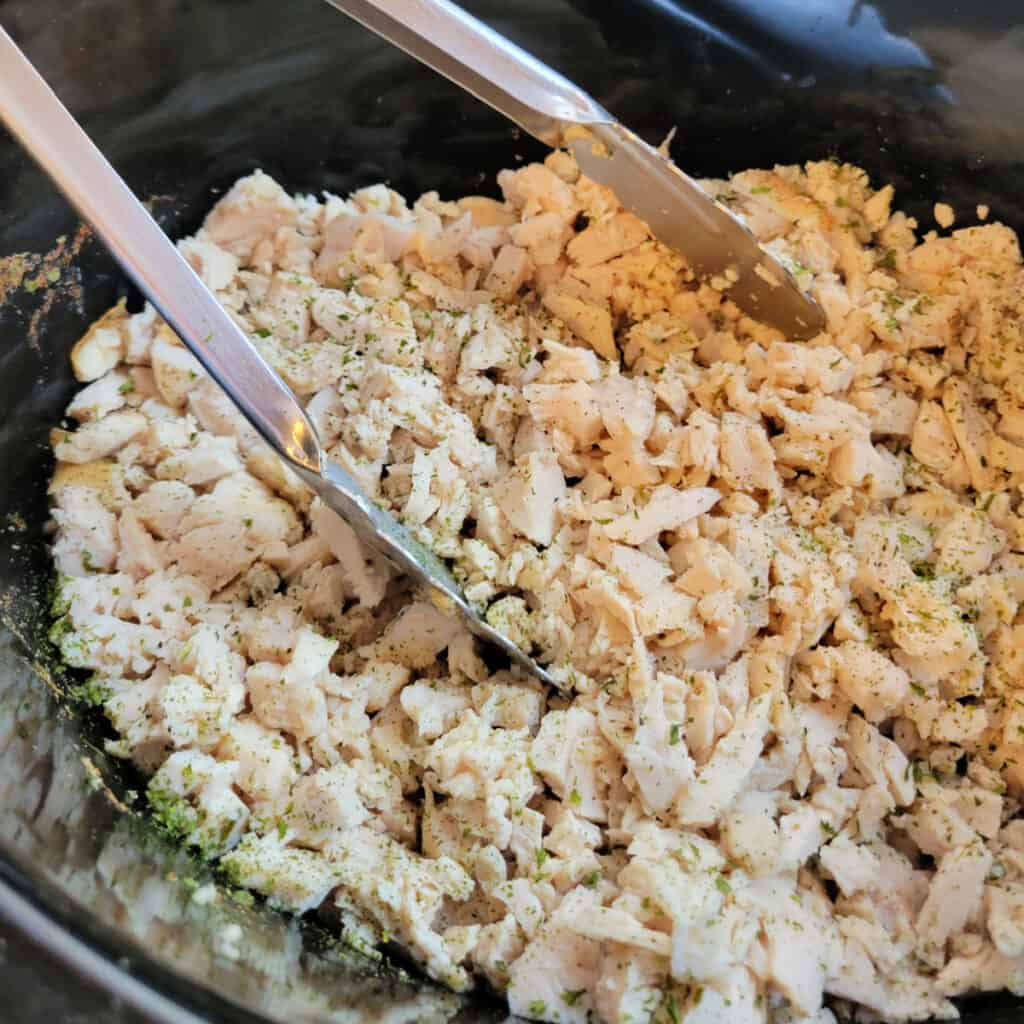 Healthy Pulled Chicken Recipe: close up of healthy pulled chicken in a slow cooker with tongs.