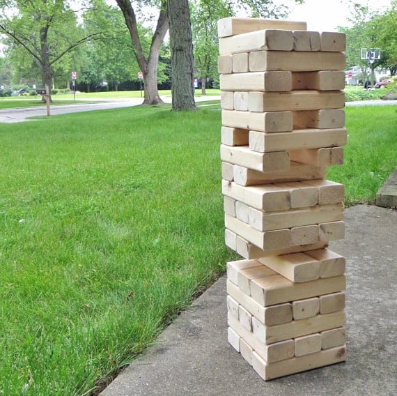 Giant jenga blocks pictured on concrete next to green grass.
