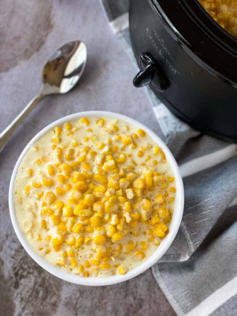 Slow Cooker Creamed Corn in a white serving bowl next to a spoon.