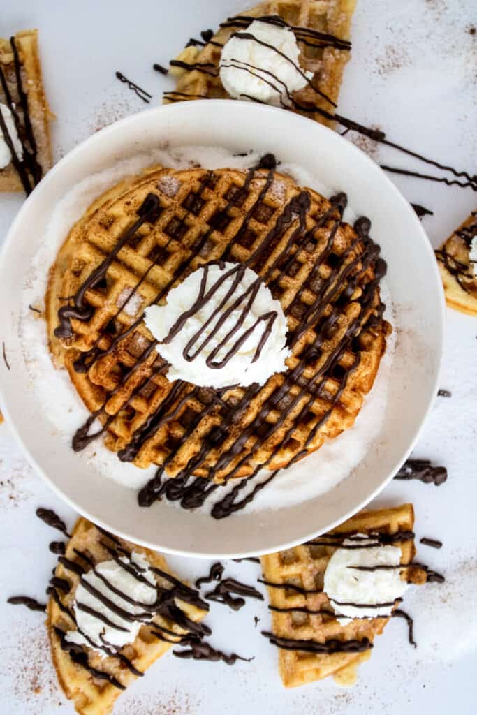 Top down view of cinnamon sugar waffles topped with whipped cream and drizzled with chocolate sauce.