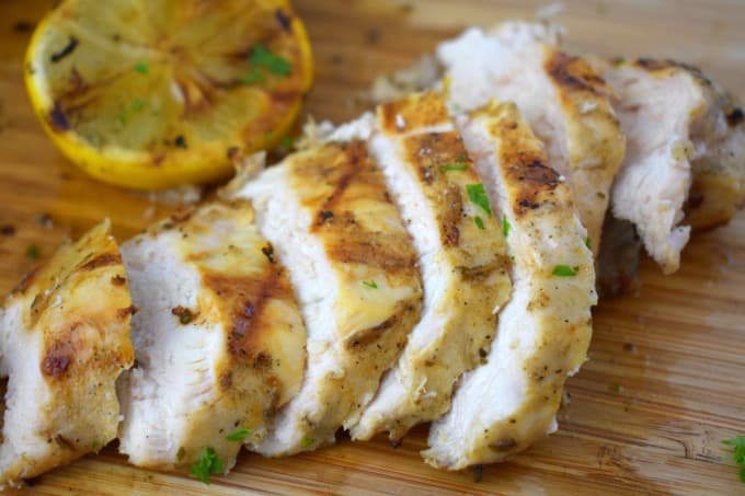 A close up of lemon garlic grilled chicken cut into slices on a cutting board cut.