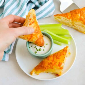 Hand holding a Buffalo Chicken Puff Pastry Pocket dipping into ranch dressing.