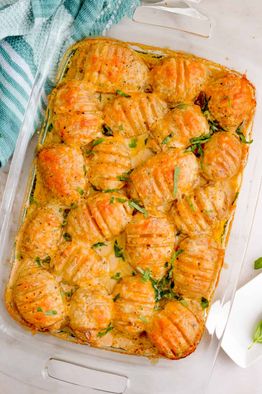 Top down view of Cheesy Hasselback Potatoes garnished with fresh basil in a casserole dish.