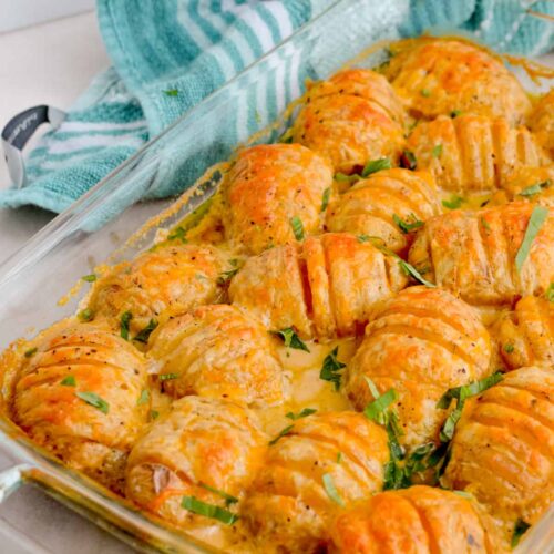 Cheesy Hasselback Potatoes garnished with fresh basil in a casserole dish.