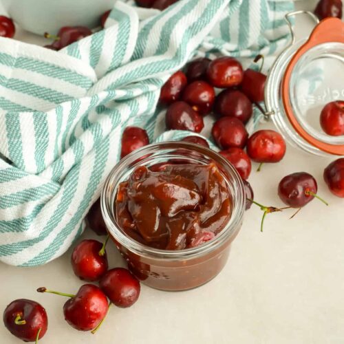 Jar of Cherry BBQ Sauce surrounded by fresh cherries.