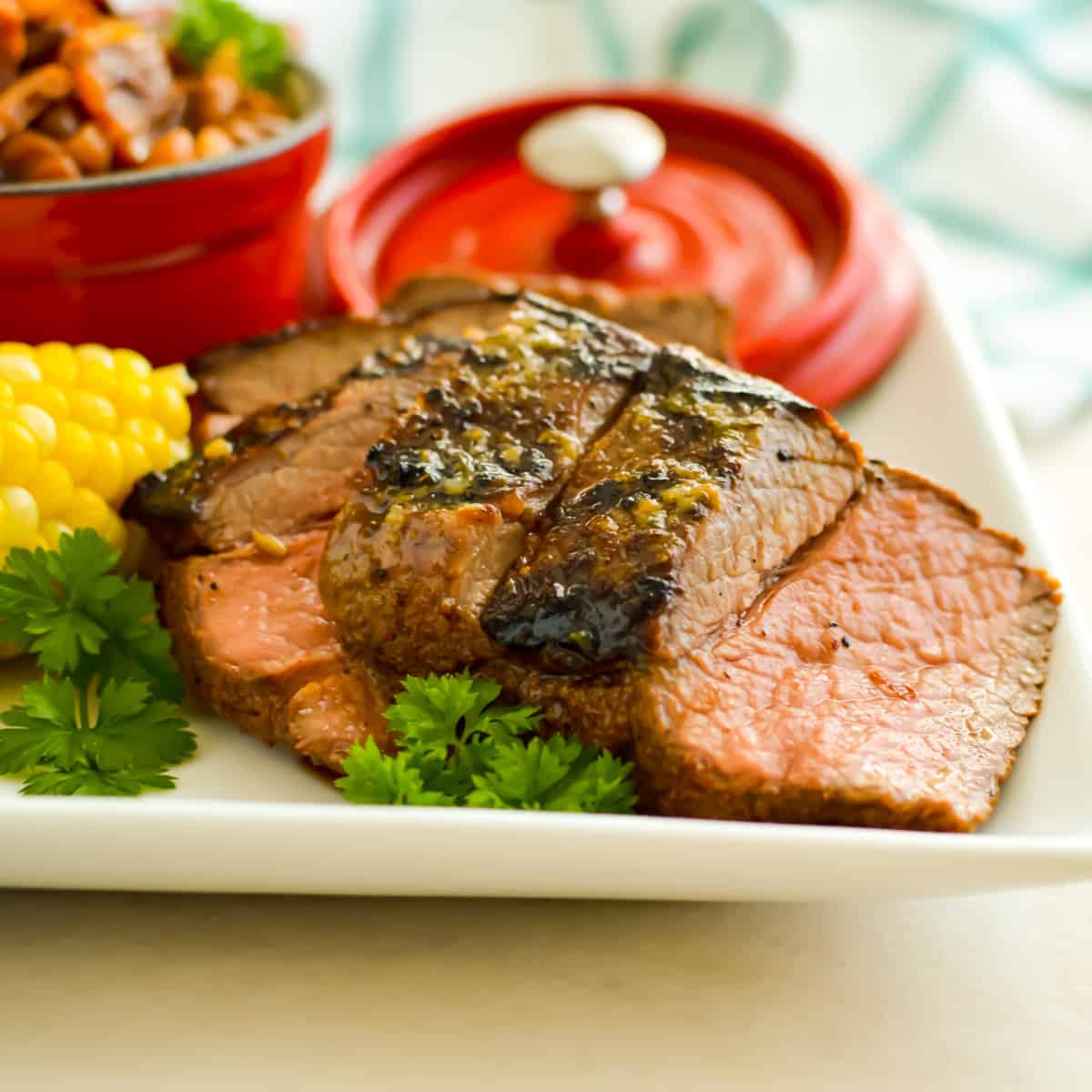 Sliced Grilled Top Sirloin Steak on a white plate with herbs.