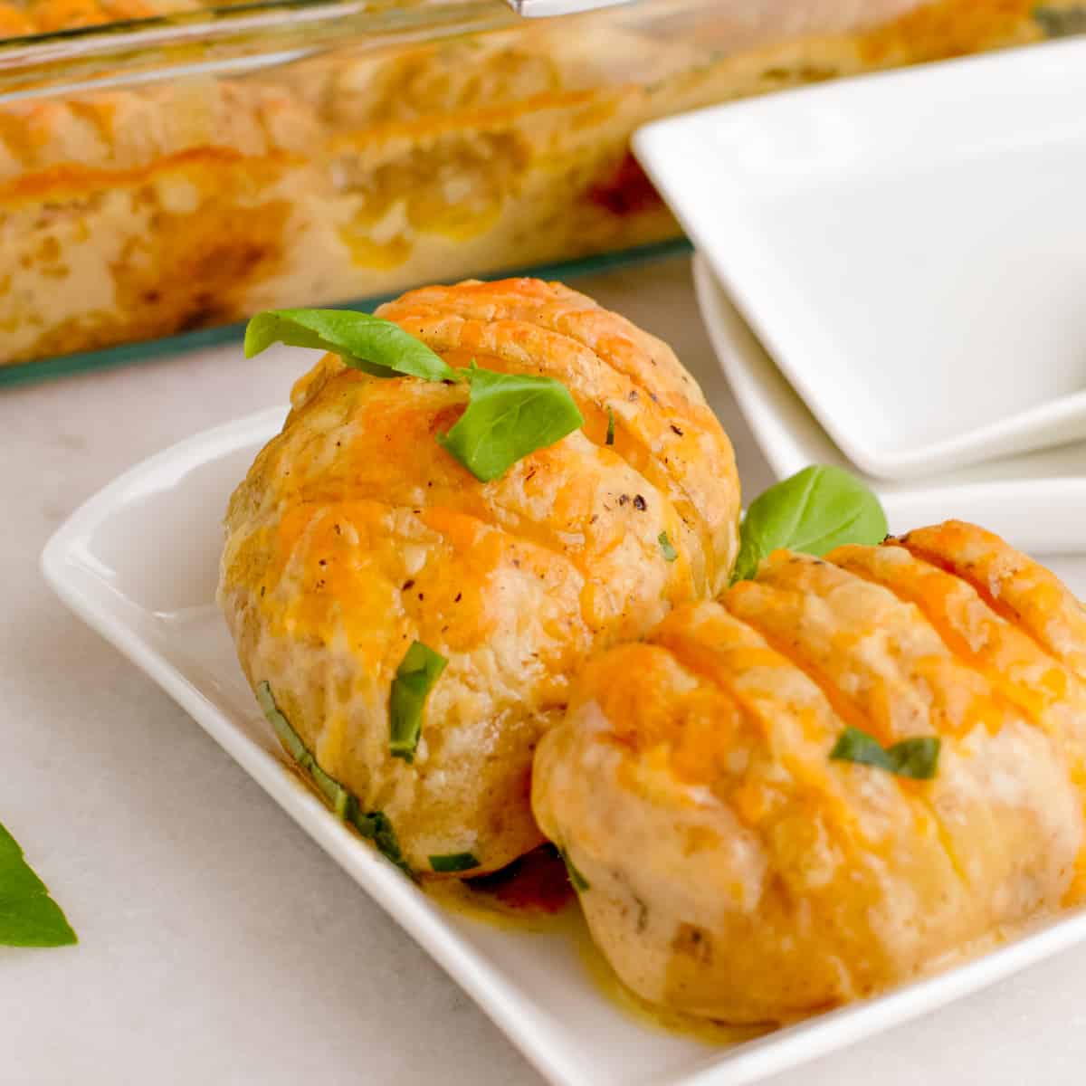Close up of Cheesy Hasselback Potatoes garnished with fresh basil on a white plate.