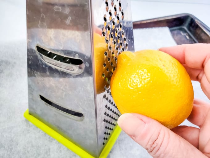Hand holding a fresh lemon against a box grater.