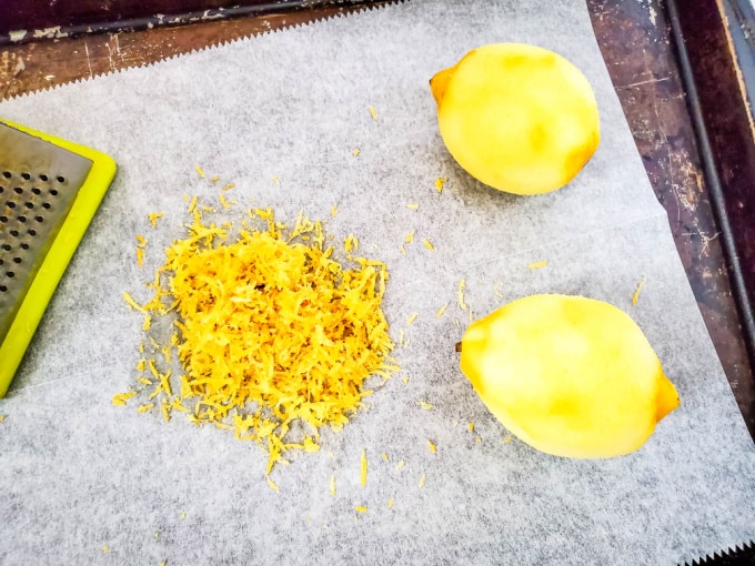Lemon zest on parchment paper next to two zested lemons.