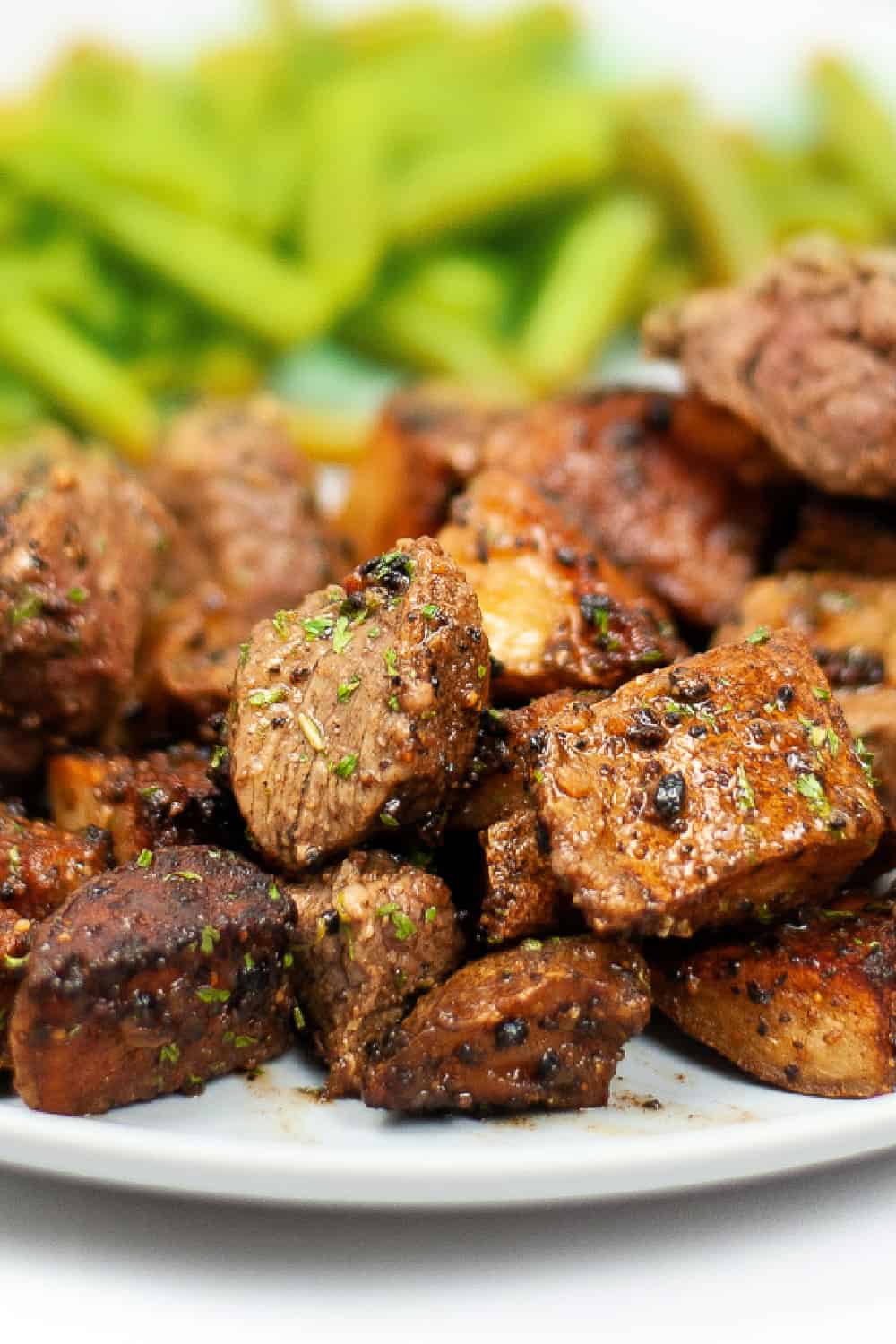 Vertical image of Steak Bites and Potatoes on a white plate with green beans.