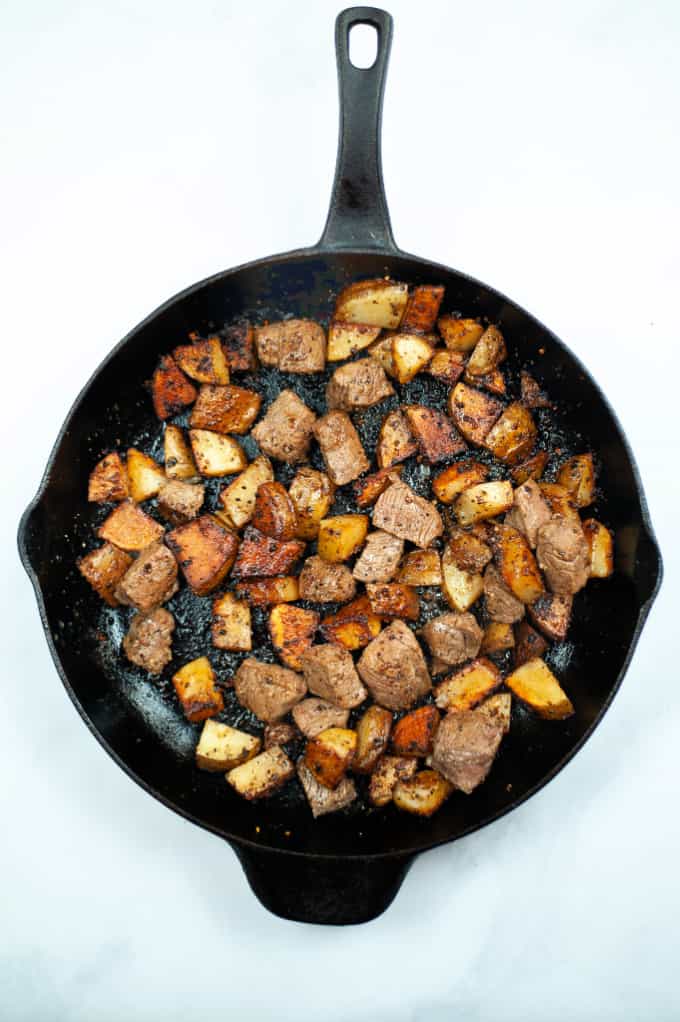 Top down view of Close up of Steak Bites and Potatoes in a cast iron skillet.