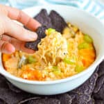 Close up of a hand scooping Cheesy Buffalo Chicken Dip with blue corn chips.