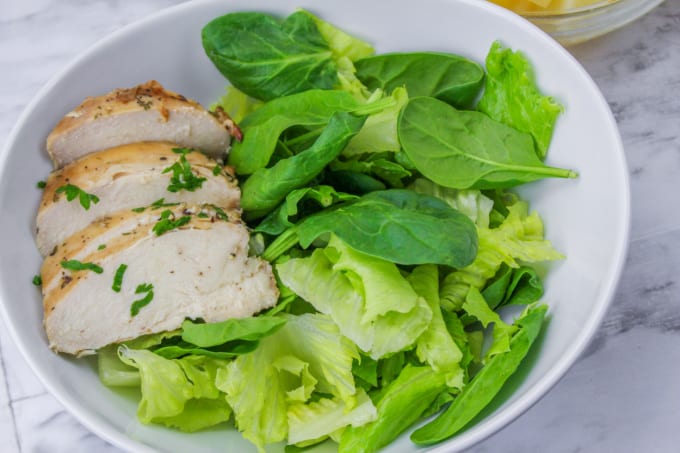 Lettuce, spinach and slices of chicken in a white bowl.
