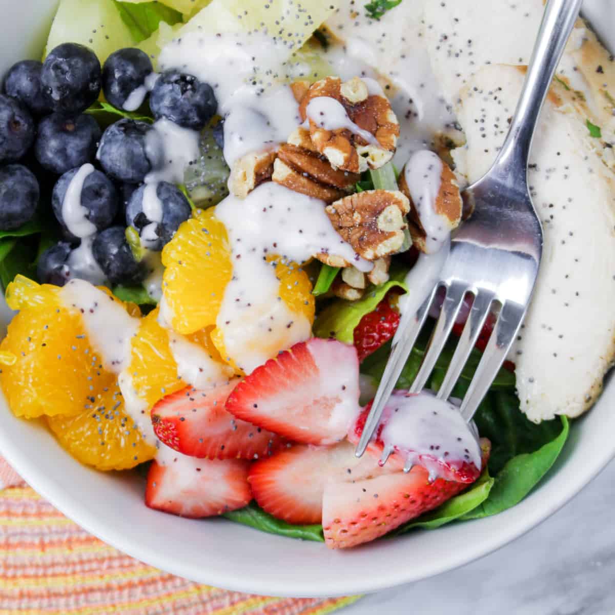 Close up of Bowl of Copycat Panera Strawberry Poppyseed Salad with chicken, fruit and nuts.