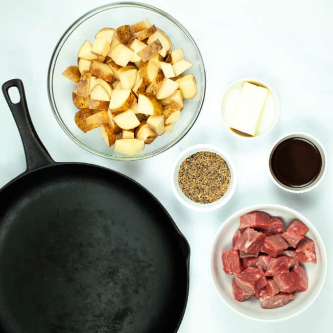 Top down view of skillet, potatoes, steak, and seasonings.