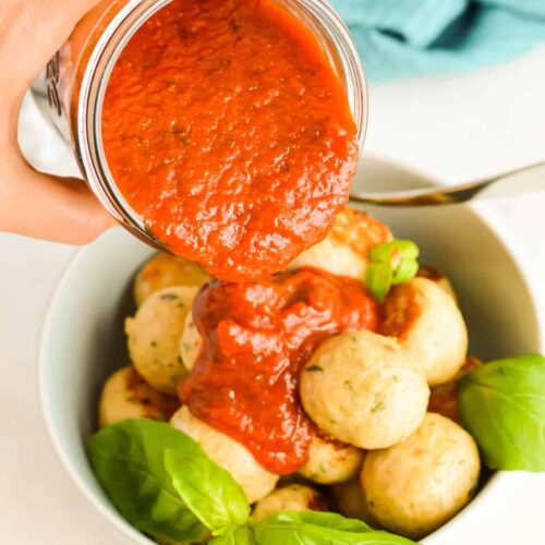 Close up of tomato sauce being poured over Italian Chicken Meatballs.