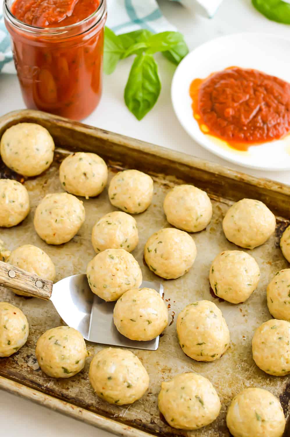 Sheet pan of Italian Chicken Meatballs next to a jar of tomato sauce.