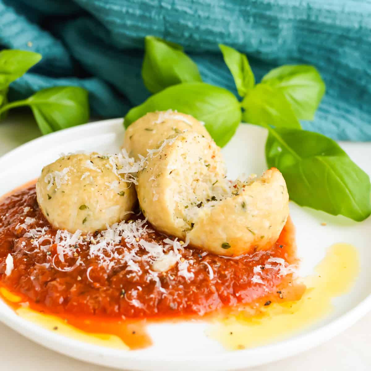 Close up of juicy chicken meatballs on a plate with tomato sauce and fresh basil.