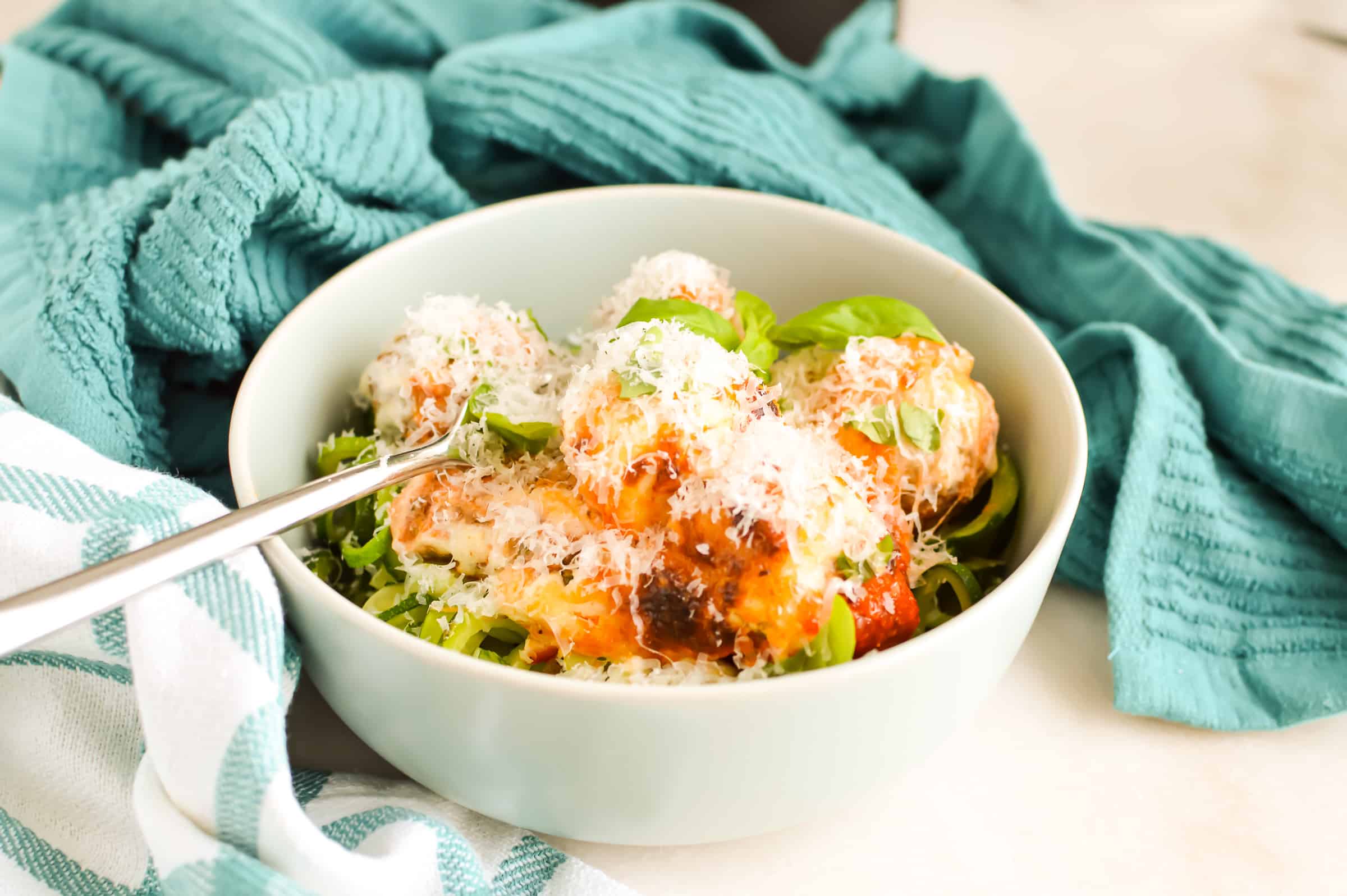 Cheesy Meatball Casserole with a white bowl with zucchini noodles.
