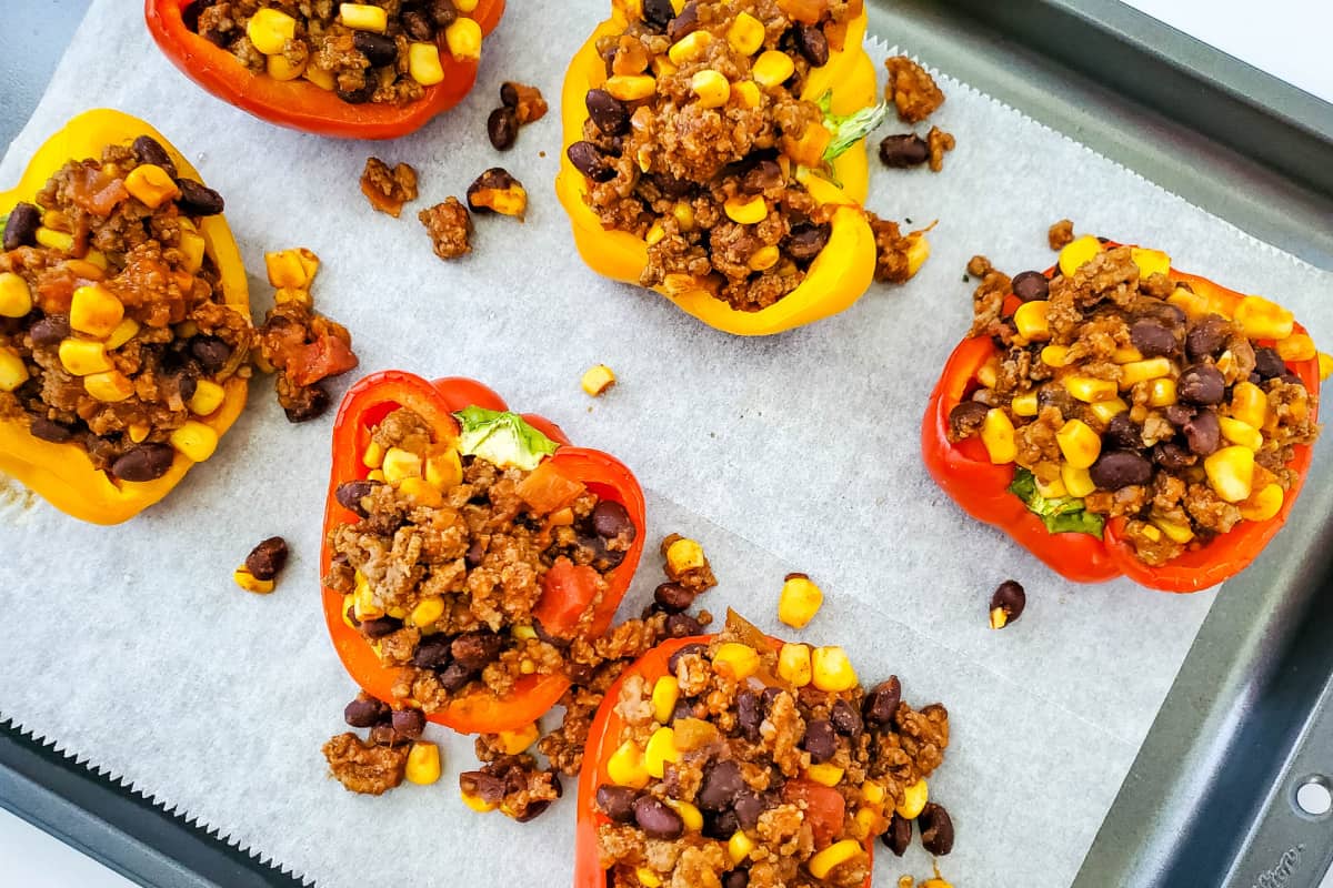 Red and bellow Stuffed Peppers on a parchment paper lined baking sheet.