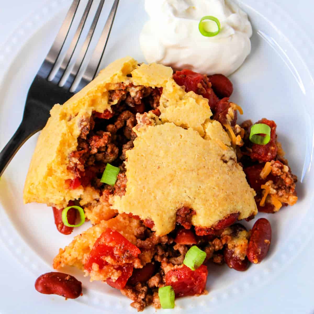 Close up of chili cornbread casserole on a white plate with a fork.