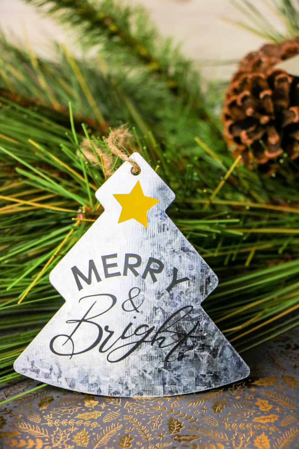Cricut Galvanized Christmas Ornament leaned against pine needles.
