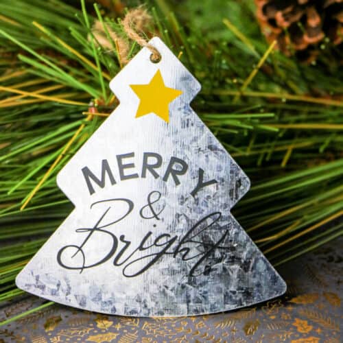 Cricut Galvanized Christmas Ornament leaned against pine needles.