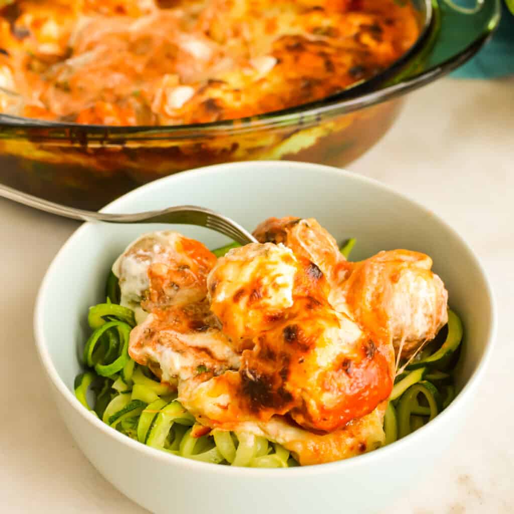 Close up of Cheesy Meatball Casserole on top of a bowl of zuchcini noodles.