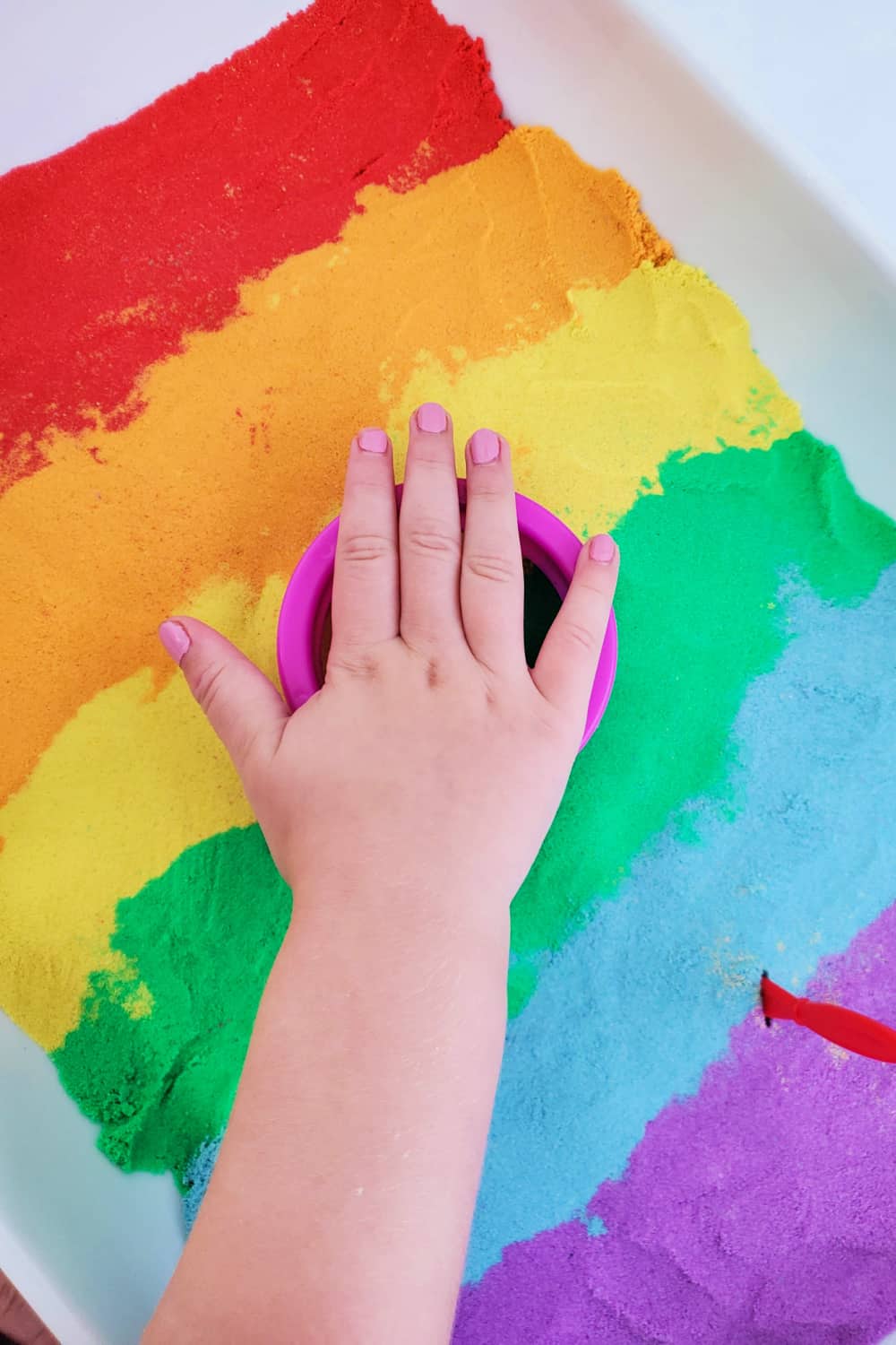 Child's hand playing with kinetic rainbow sand.