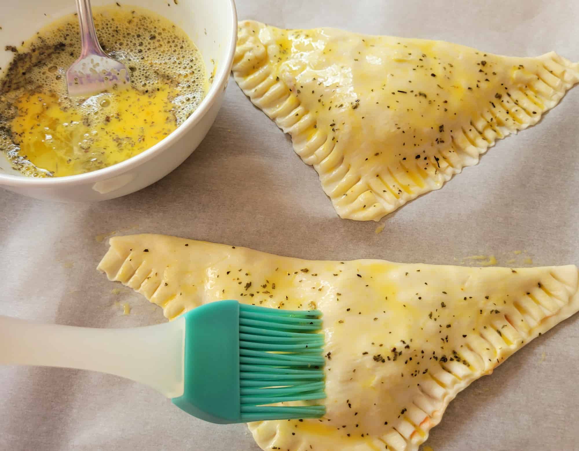 Close up of egg wash being brushed onto puff pastry pockets.